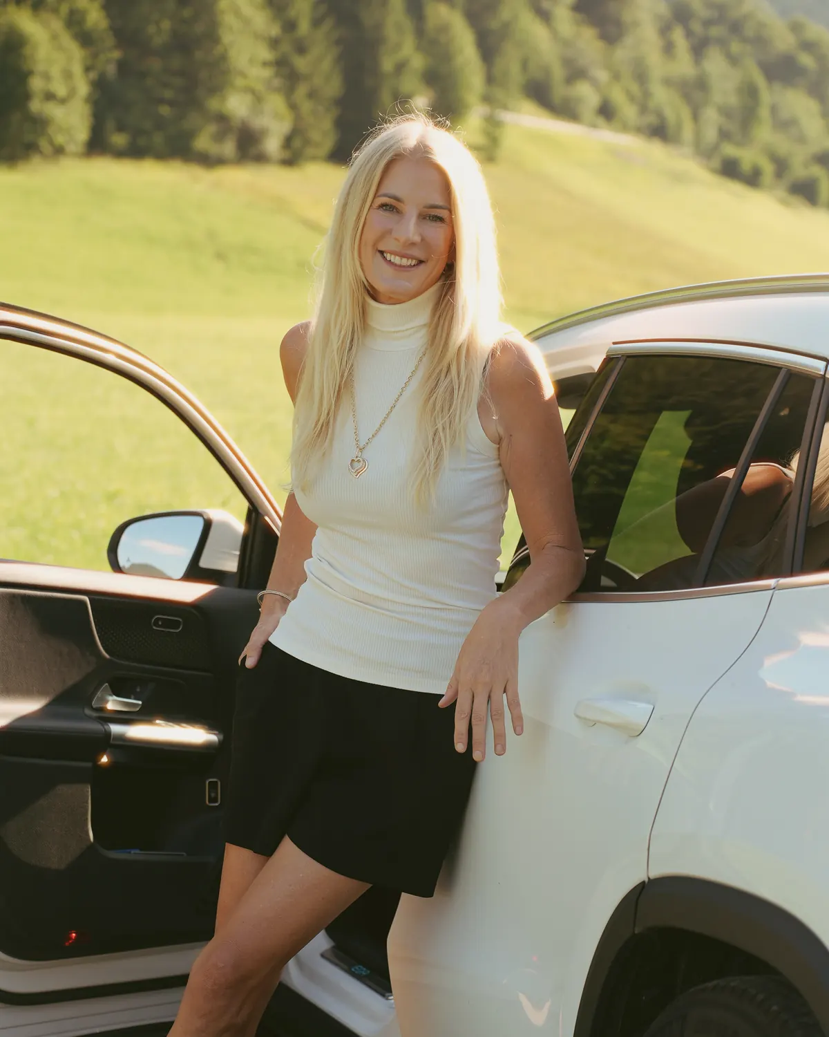 Maklerin von Alpen Immo mit weißem E-Auto in den Bergen